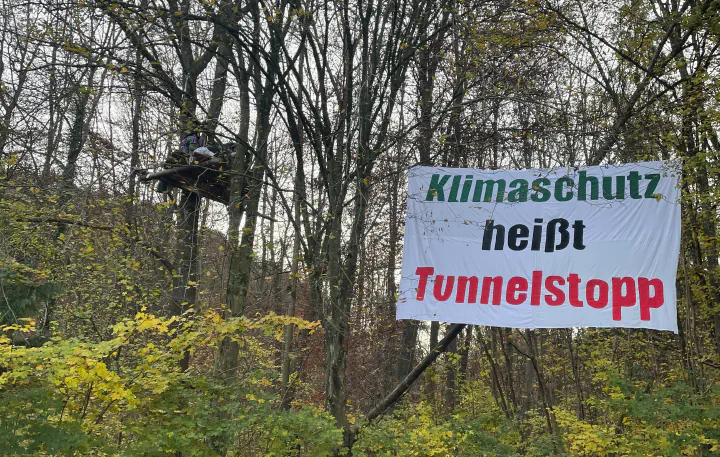 Ein einfaches Baumhaus hängt im Wald, dazu ein Banner mit der Aufschrift "Klimaschutz heißt Tunnelstopp"